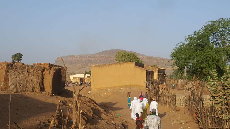 A tall mountain called Mount Tapa is in the background with people walking toward it in Mali.