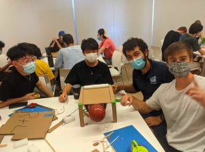 Students in masks working on a project face the camera and smile.