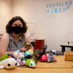 Maria Palmtag sits at a table in the BeAM makerspace surrounded by stuffed animals.