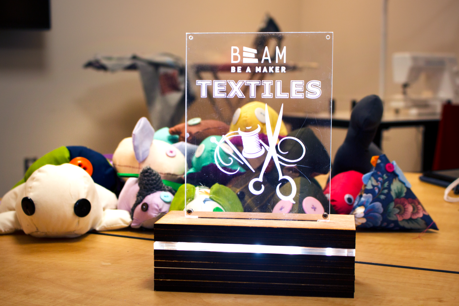 Stuffed animals and a custom-made lamp with a BeAM textiles logo sit on a table.