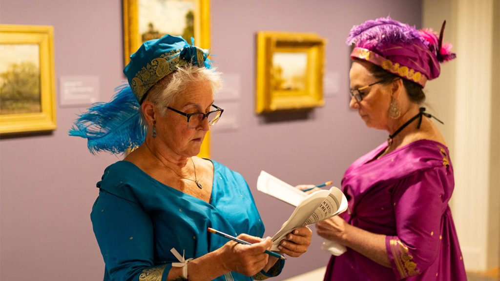 Two women dressed in Regency regalia take notes in the Ackland Art Museum.