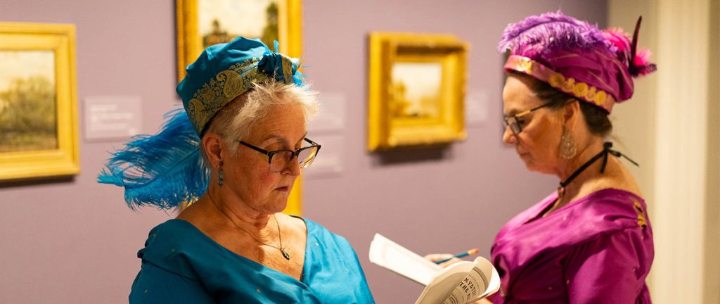 Two women in Regency regalia stand talking at the Ackland Art Museum at the Jane Austen event.