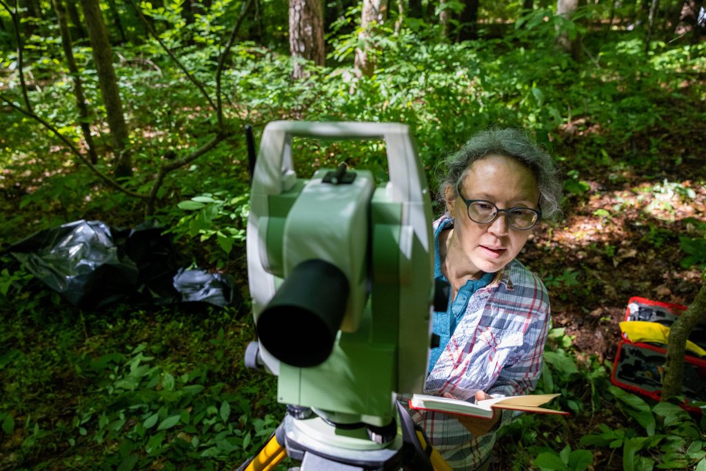 Heather Lapham peeks around a giant instrument as she stand in the forest making measurements.