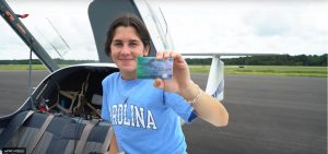 Paige Court holds pilot's license in front of a plane.