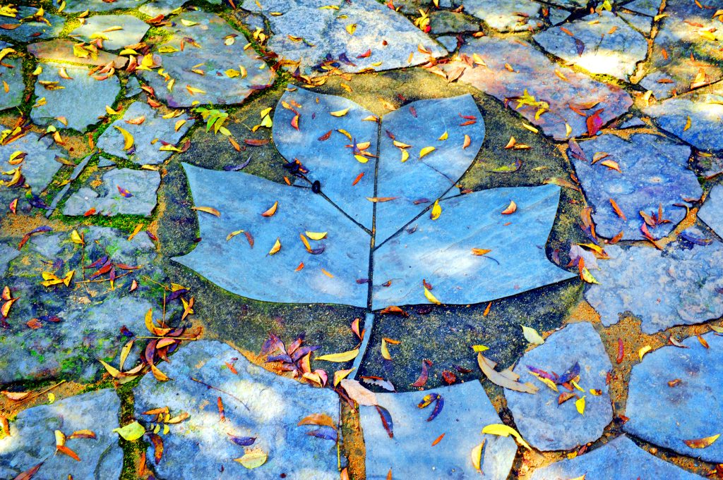 A sculpture made of blue leaves lies on the ground with colorful real fall leaves around it.