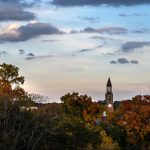 The bell tower in the distance surrounded by fall foliage.