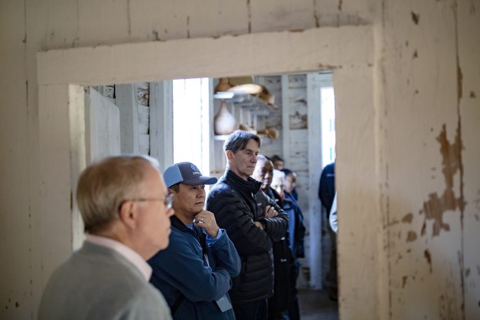 A line of people, including Nianbo Dong and Jim White, stand in the Somerset Place, listening during a tour.