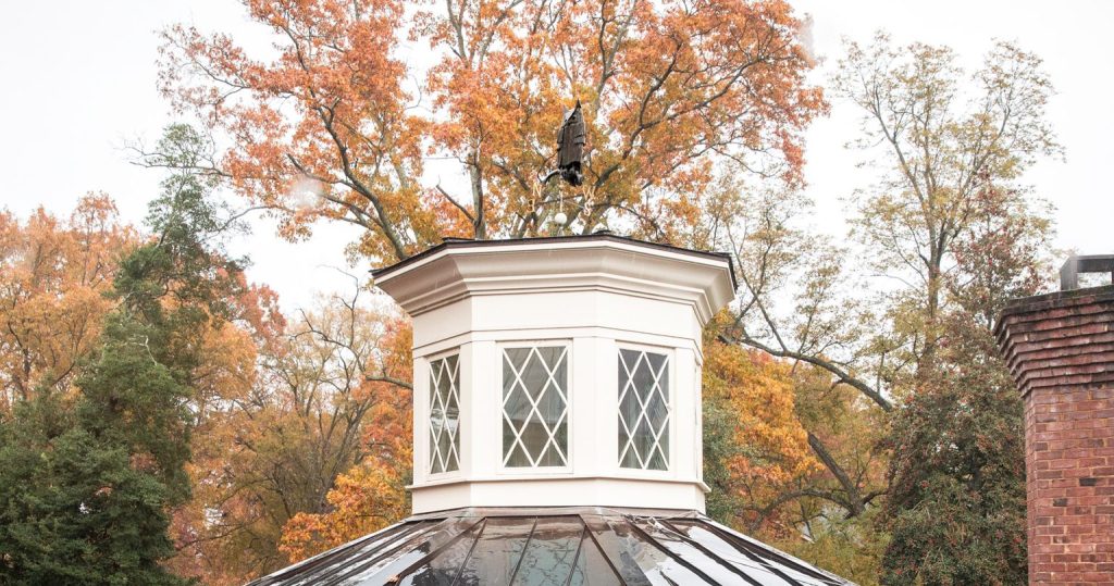 The cupola of Hyde Hall with fall foliage behind it. On top of the cupola is an small owl.