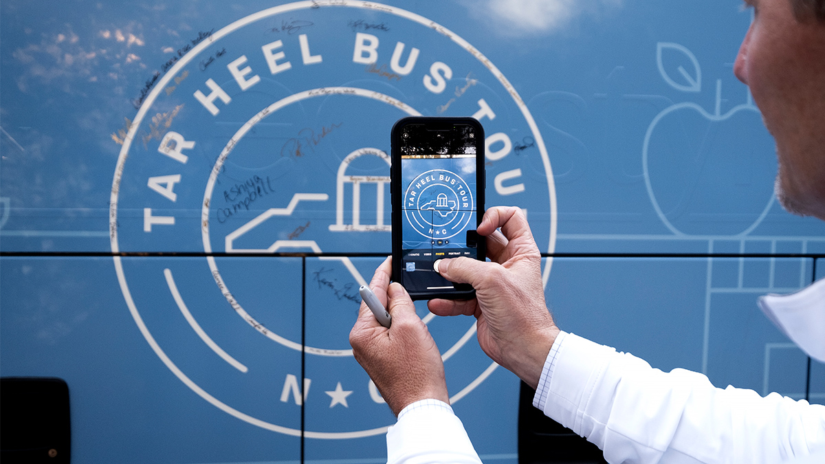A person takes a picture of the signatures on one of the buses from the 2022 Tar Heel Bus Tour with their phone.