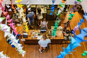 The camera looks down at Meantime Coffee through the collection of brightly colored origami cranes.