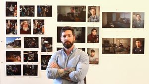 Matthew Troyer crossing his arms in front of a collage of photos he's taken as a combat photographer.