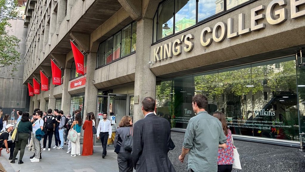 Rudi Colloredo-Mansfeld, Will Wootton and Emma Bishop walk toward the KCL Strand building, a big stone building with a crowd of students outside.
