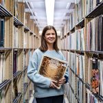Caroline Norland stands between the Music Library's stacks holding a record of the composer Handel.