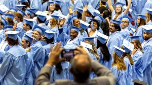 A crowd of waving Carolina Winter graduates in their blue caps and gowns.