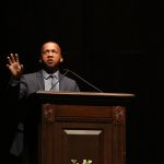 Bryan Stevenson wears a suit and speaks into a microphone at a podium.