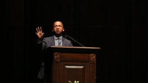 Bryan Stevenson wears a suit and speaks into a microphone at a podium.