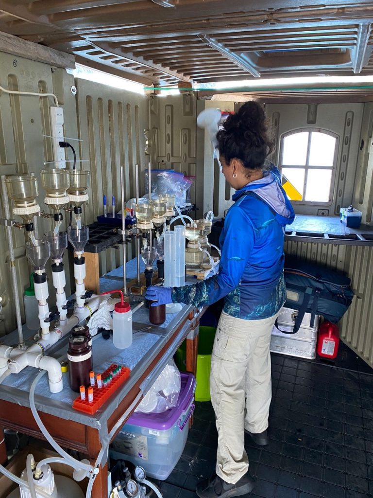 Cristina Vintimilla stands at a table covered in lab equipment, including beakers, plastic containers and plastic piping.