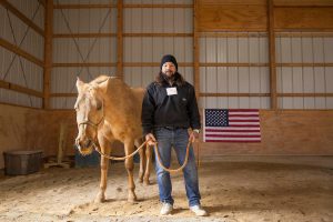 Matthew Colon stands in a barn with a horse, holding its reins.