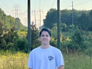 Jake Otte standing outside in front of a substation, phone lines and trees in the background.