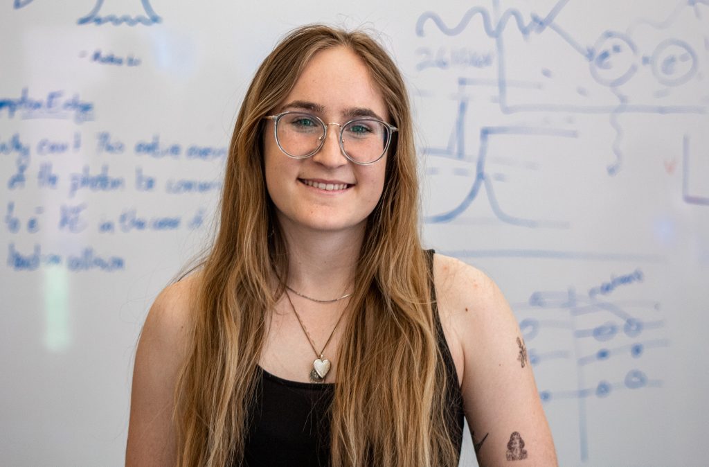 Sarah Vickers stands in front of a whiteboard with notes and equations on it in her physics lab.