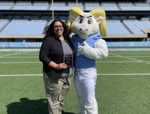 El Fisseha, holding up a plaque, poses with UNC mascot Ramses on the Kenan Stadium field.