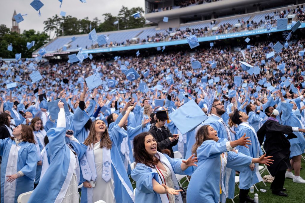 A sea of graduates in Carolina blue caps and gowns fill the field at Kenan Stadium.