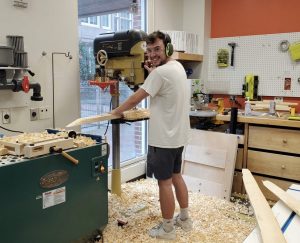 Cy Pair stands surrounded by wood tools and other tools in the woodshop of the BeAM makerspace.