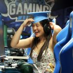 Emma turns her head to the side and nods, wearing her graduation cap, in the Carolina Gaming Arena.