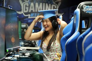 Emma turns her head to the side and nods, wearing her graduation cap, in the Carolina Gaming Arena.