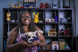 Priscilla Layne holds a Lego creation she built. Behind her is a shelve full of Lego creations.