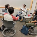 A team of Ph.D. students sits in a circle in chairs, brainstorming ideas.