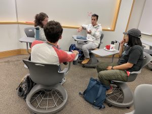 A team of Ph.D. students sits in a circle in chairs, brainstorming ideas.