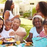 An African-American family gathers around the table for dinner. The dinner is outside.