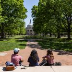 Three students sit on the steps on UNC's South Building, overlooking the trees on the main quad.