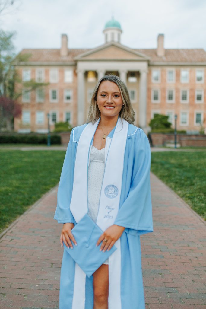 Erin Storch wears her Carolina blue graduation gown in front of South Building on UNC's campus.