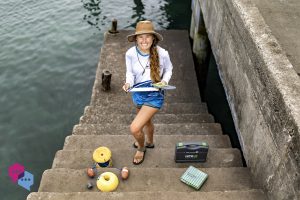 Savannah Ryburn stands on steps leading down to the water. She is holding a clipboard and wearing a hat.