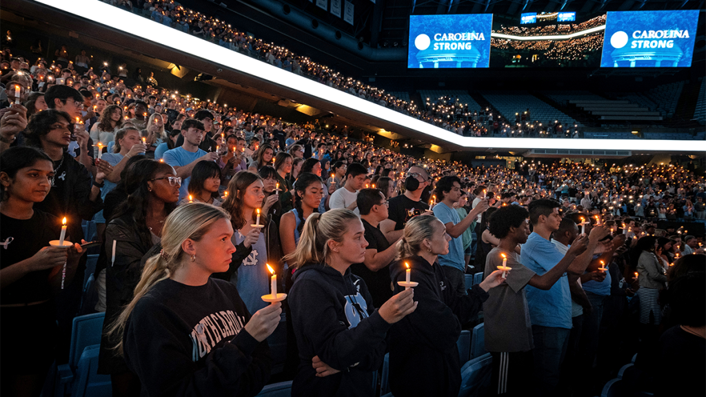People hold candles in the darkness of the Dean Smith Center.