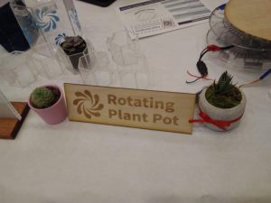 A sign on a table between two potted plants reads: "Rotating Plant Pot."