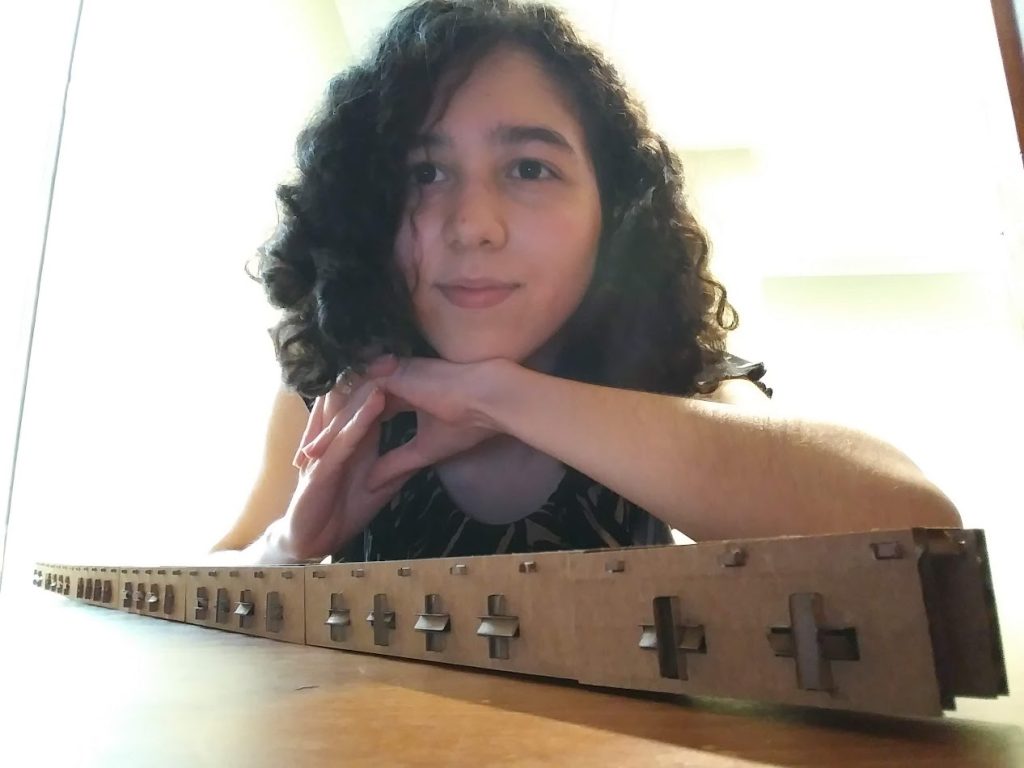 Daniella Martinez Leal smiles at the camera as she leans on a cardboard bridge creation.