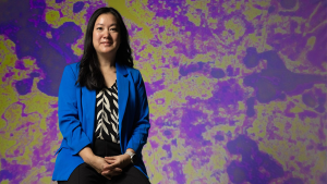 Professional waist-up shot of Angel Hsu in front of a mottled green and purple background.