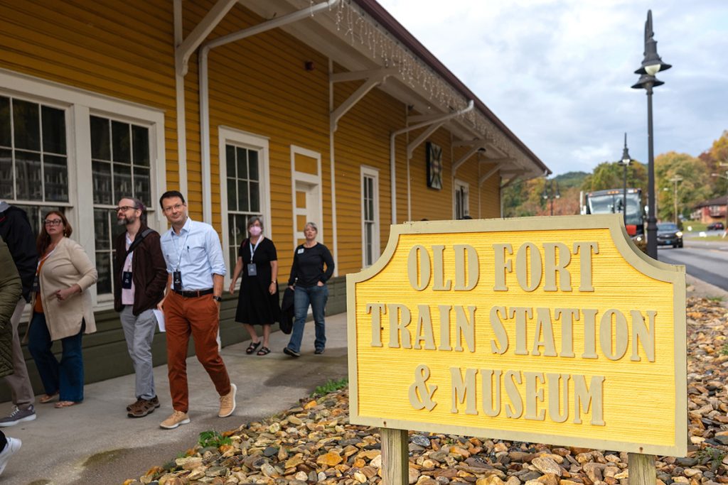 Tar Heel Bus Tour participants walk by a sign that says "Old Fort Train Station and Museum."