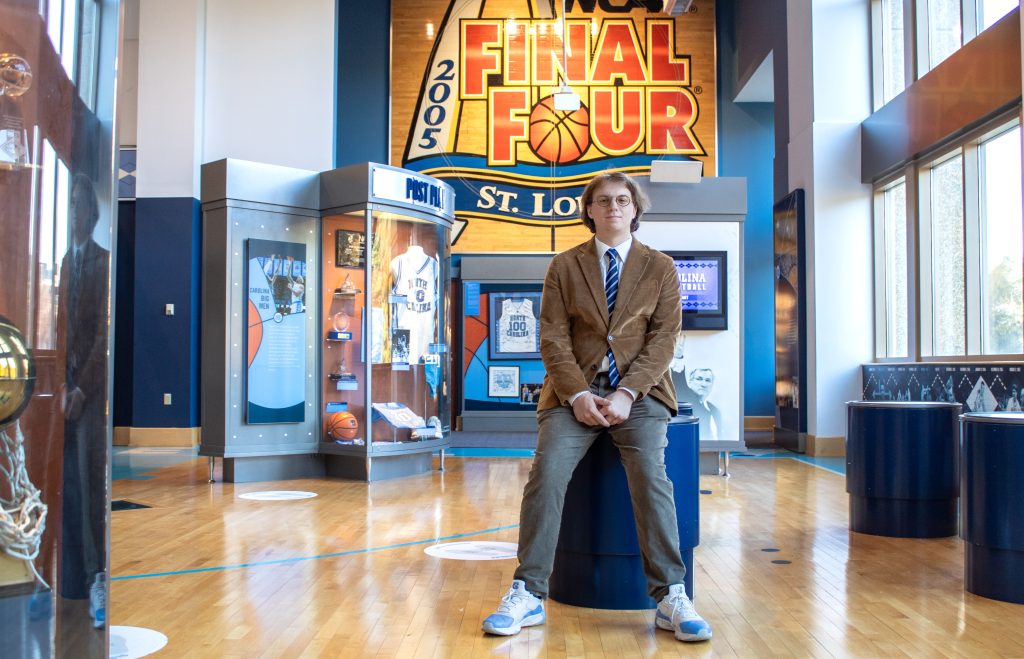 Conor Kerr sits in front of exhibits at the Carolina Basketball Museum.