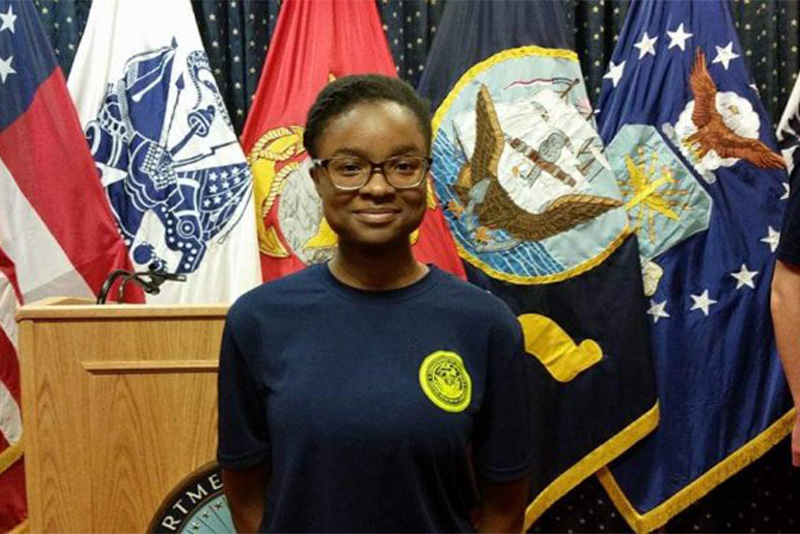Kaela Hunter posing in front of flags while wearing a Navy blue sweatshirt with a U.S. Navy emblem.
