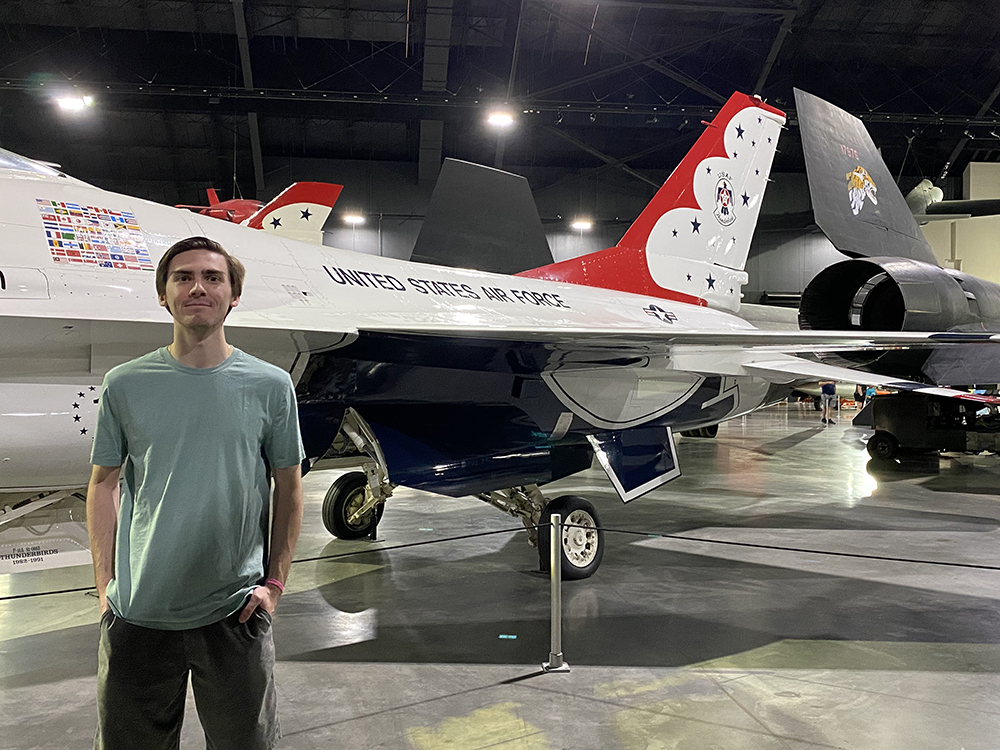 John Migliore stands in an airplane hangar in front of a "United States Air Force" craft. 