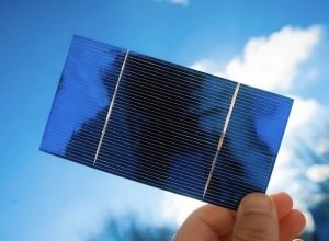 A hand holds up a perskovite solar cell, a roughly hand-sized dark blue panel, to the sky