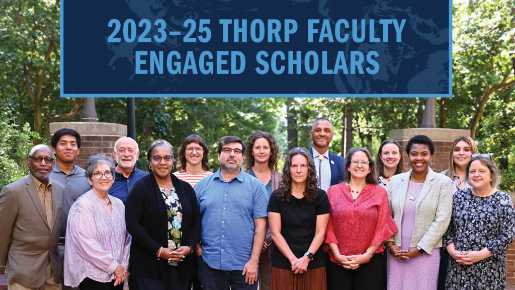 A group photo of 15 faculty members posing outside in front of a brick wall with trees behind them. A banner reading "2023-25 Thorp Faculty Engaged Scholars" is at the top of the image.