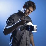 Richard Marks holds up a PlayStation VR headset with his pointer finger, examining it.