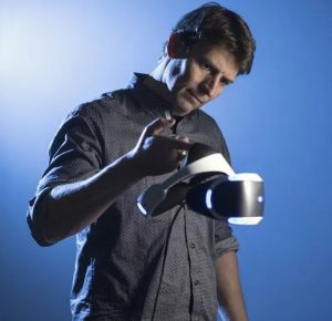 Richard Marks holds up a PlayStation VR headset with his pointer finger, examining it.