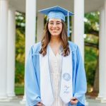 Headshot of Emma Cohn in her Carolina blue graduation cap and gown, the Old Well in the background.