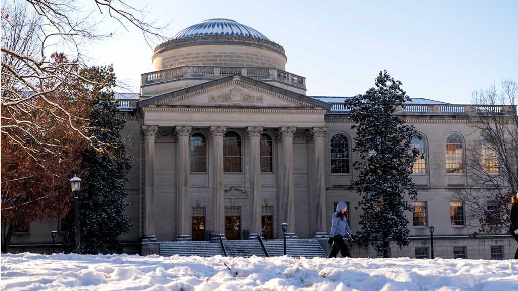 A student walks in front of Wilson Library in the snow.
